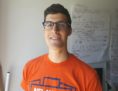 Gabriel Fontes headshot. Gabriel is wearing an orange T shirt, with a flipchart in the background. 