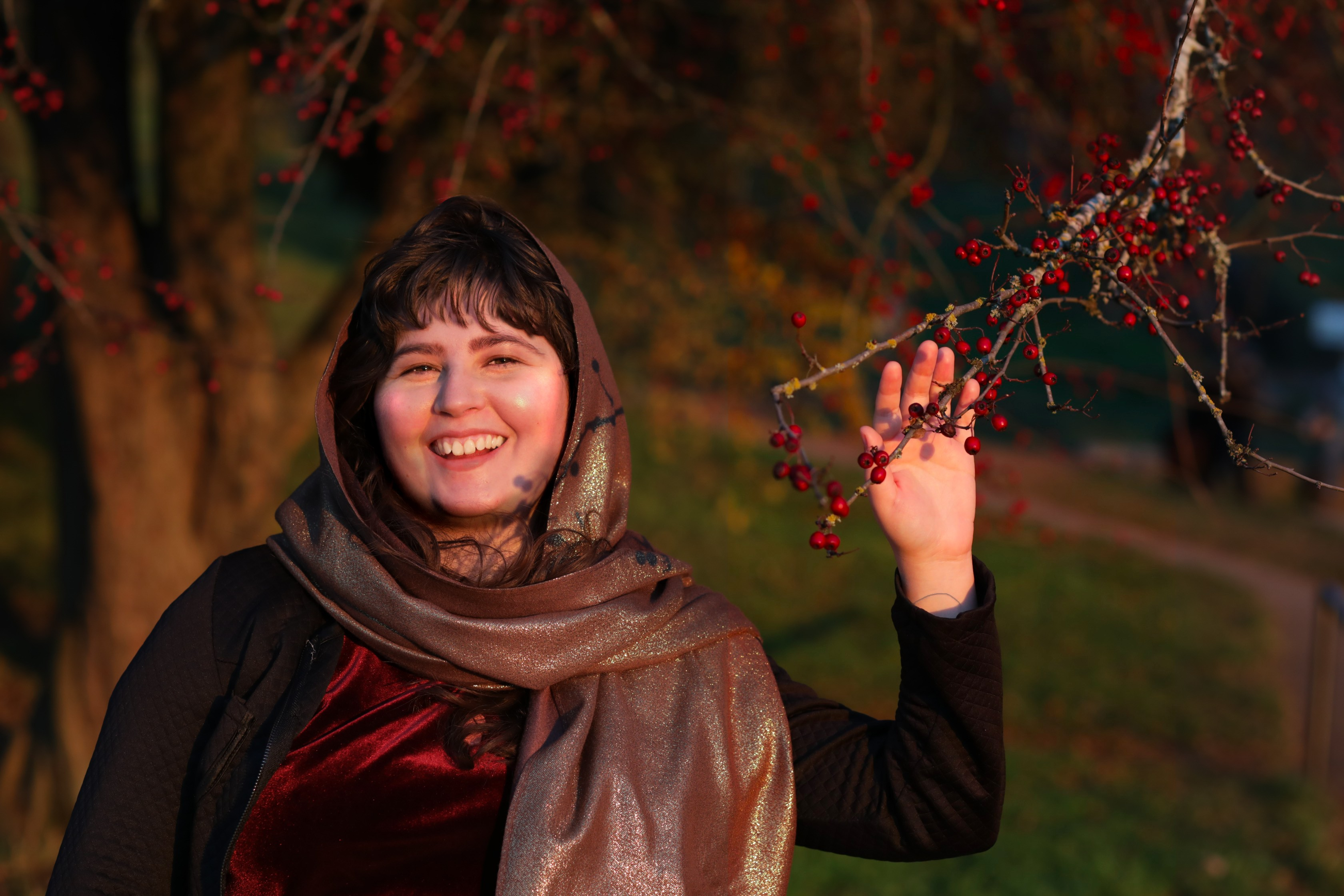 photo of Sahar L. Jones in front of a tree with the hand reaching for a branch with red berries