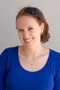 photo of Emily Holtzman, a white women with auburn hair in a blue top and black flower headband