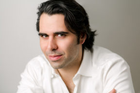 Headshot of Joseph Flaxman, white man with dark hair wearing an open collared white button up shirt against a light gray background looking directly into the camera.