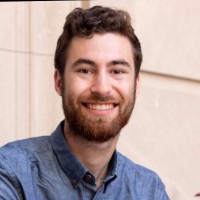 Headshot of Avidan smiling, with brown hair and a reddish beard, wearing a blue button-down shirt. 