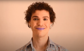 A person with brown curly hair, purple lipstick, earrings and a blue floral shirt.