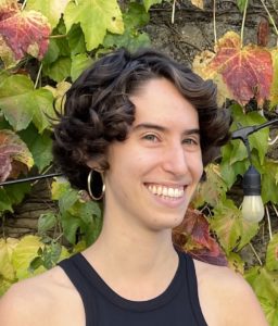 Headshot of white woman with short curly brown hair smiling away from the camera