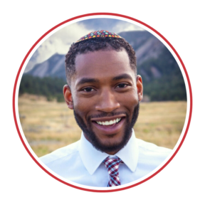 Headshot of Bryant Heinzelman, a black man, wearing a kippah, a white shirt and a tie standing in a mountain range setting.